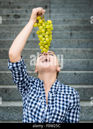 Young woman eating grapes outdoor sitting on stairs Stock Photo