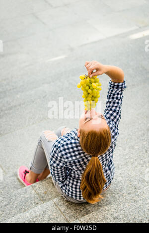 Young woman eating grapes outdoor sitting on stairs - above view Stock Photo