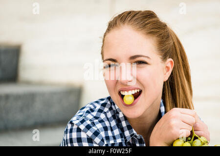 Young woman eating grapes outdoor - holding grape between teeth Stock Photo