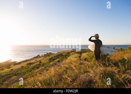 Rear view of young male surfer looking out to sea from clifftop Stock Photo