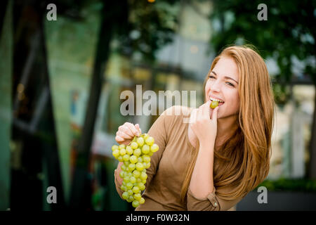 Young woman - teenage girl eating grapes outdoor in street Stock Photo