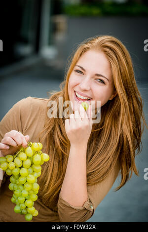 Young woman - teenage girl eating grapes outdoor in street Stock Photo