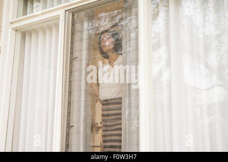 Mid adult woman looking out of house window Stock Photo