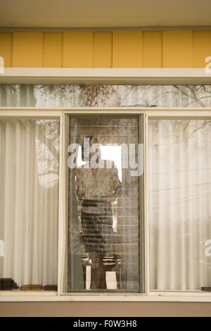 Woman looking out of house window Stock Photo