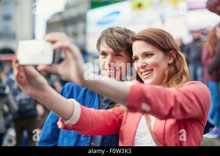 Tourist couple taking smartphone selfie at Piccadilly Circus, London, UK Stock Photo