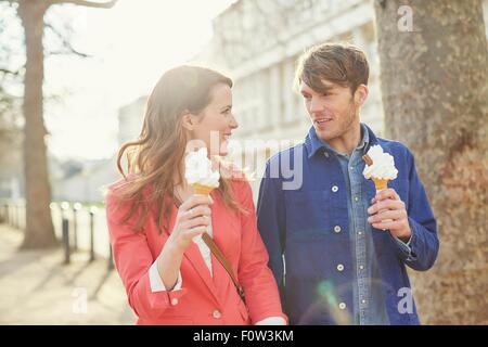Couple eating ice cream cones whilst strolling along street, London, UK Stock Photo