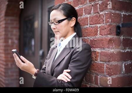 Businesswoman using smartphone next to brick wall Stock Photo