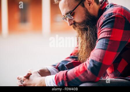 Side view of man with beard wearing sunglasses looking down Stock Photo