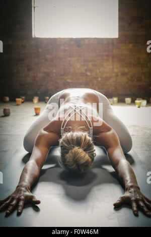 A blonde woman in a white crop top and leggings, bending down on a yoga mat surrounded by candles, doing yoga. Stock Photo