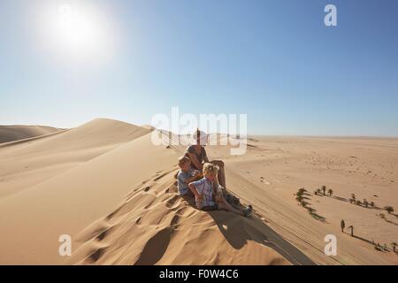 Mother and sons sitting on sand dune, Dune 7, Namib-Naukluft National Park, Africa Stock Photo