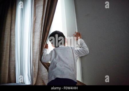 Boy peeking out from curtain Stock Photo