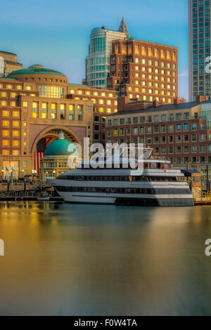 Boston Harborwalk Daybreak - A view during sunrise to Rowes Wharf, the Boston Harbor and skyline.  Seen is the Odyssey Cruise Yacht, along with other high rises along the waterfront. Stock Photo