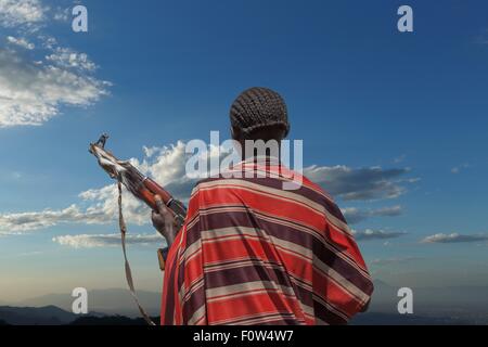 Rear view of young man from Karo tribe with Kalashnikov rifle, watching his herd , Ethiopia, Africa Stock Photo