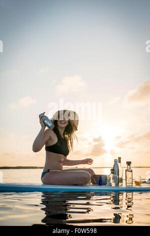 Young woman preparing cocktails on paddleboard at sunset, Islamorada, Florida, USA Stock Photo