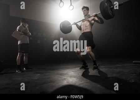 Mid adult man lifting barbell, while trainer looks on, low angle view Stock Photo