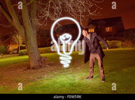 Artist light painting a lightbulb symbol in park Stock Photo