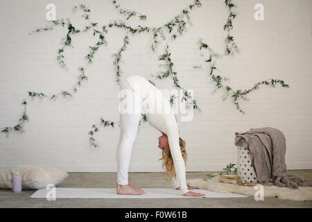 A blonde woman  bending forward to the floor, stretching her back with her hands down on the floor. Stock Photo