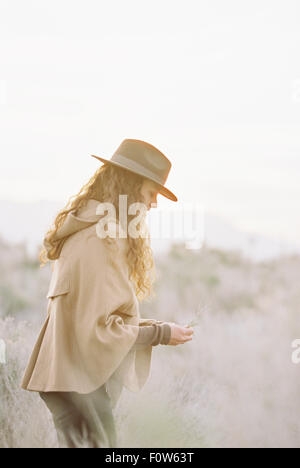 A woman in a warm coat and a hat picking wild flowers. Stock Photo