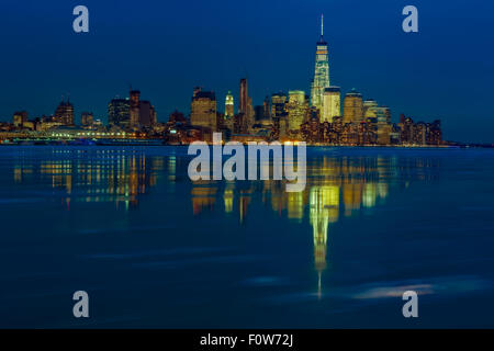 Frozen Lower Manhattan NYC - The lower Manhattan, New York City skyline  with One World Trade Center commonly known as the Freedom Tower along with other skyscrapers in the Financial District. The Hudson River is partially frozen on a clear but very chilly winter evening. The skyline is reflected on the open cold waters during  the blue hour after sunset. Stock Photo
