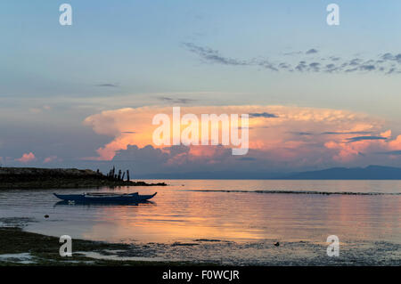 Orange Clouds Reflecting Sunlight. Early morning view at the beach. A boat left on shallow waters Stock Photo