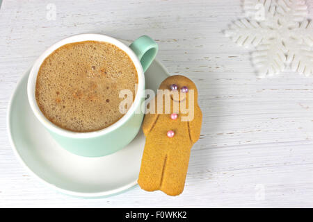 Gingerbread man and Coffee in pastel coloured cup on white rustic wooden background with snowflake. Stock Photo