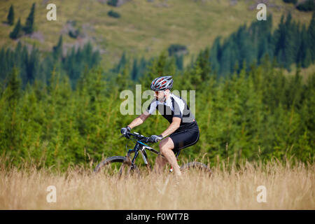 Mountain bike cyclist in sport equipment and helmet riding on rugged trails Stock Photo