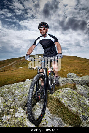 Mountain bike cyclist in sport equipment and helmet riding on rugged trails Stock Photo