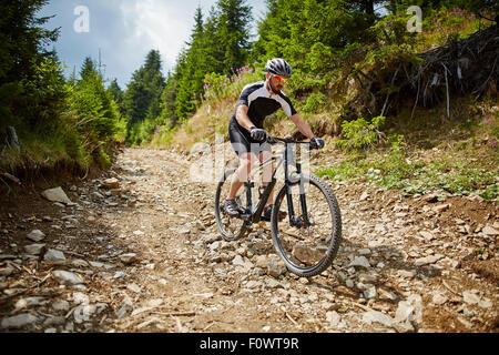 Mountain bike cyclist in sport equipment and helmet riding on rugged trails Stock Photo