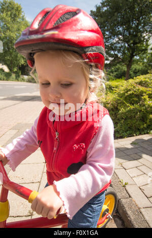 Little girl on bike on the pavement with crash helmet. Stock Photo