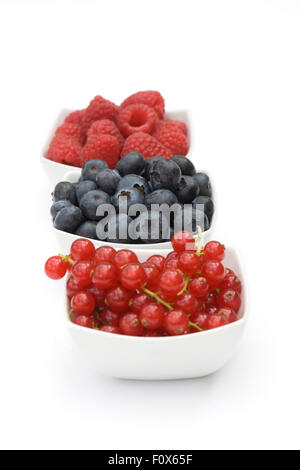 Redcurrants, Blueberries and Raspberries in white bowls on a white background. Stock Photo