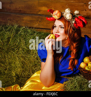 A young girl holds a ripe apple near basket with a crop of vegetables and fruit. Harvest Festival. Farm. Stock Photo