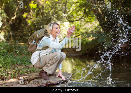 cheerful middle aged female hiker playing with stream water Stock Photo