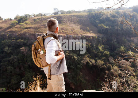 rear view of senior man with backpack standing on top of the mountain