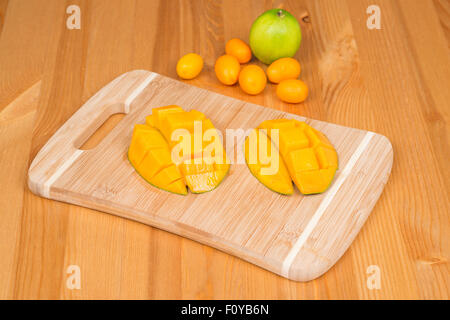 Fresh mango on a cutting board with Fresh Kumquats and a lime, on a wooden table Stock Photo