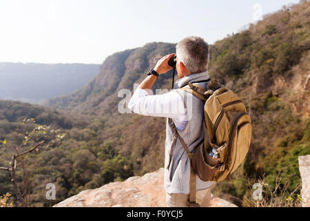 middle aged male hiker using binoculars on top of the mountain Stock Photo
