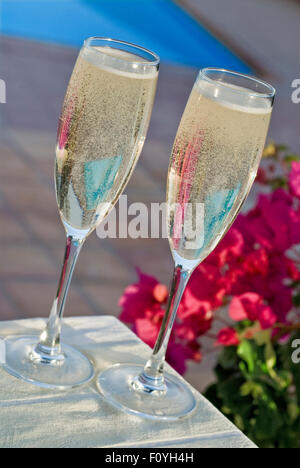 Champagne Alfresco glasses on sunlit outdoor terrace table with bougainvillea flowers and swimming pool behind luxury exotic vacation setting Stock Photo