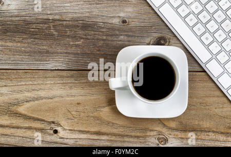 Top view of black coffee, selective focus on upper lip of coffee cup, with partial computer keyboard on rustic wood. Stock Photo