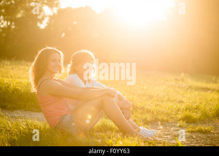 Mature mother sitting with her daughter on river bank and having great time together Stock Photo