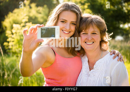 Teenage daughter and her senior mother are taking selfie photo with mobile phone Stock Photo