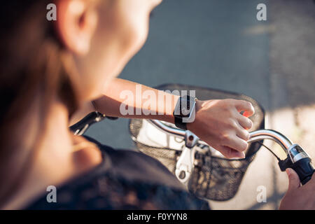 Woman with a bicycle looking at her smartwatch. Close up shot of female checking time on her smart wristwatch. Stock Photo