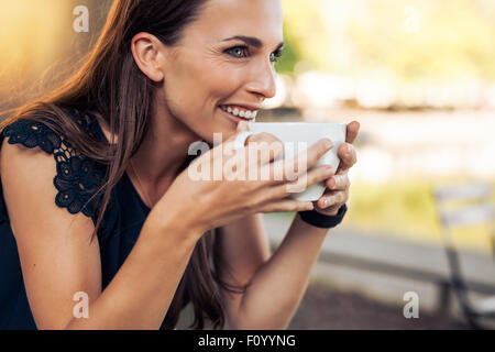 Young woman holding a cup of coffee and looking away smiling. Caucasian female drinking coffee at cafe.