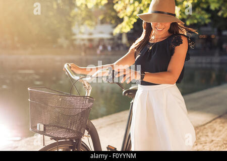 Portrait of beautiful young woman wearing a hat with a bicycle walking along a pond. Happy woman with a bike at the park. Stock Photo
