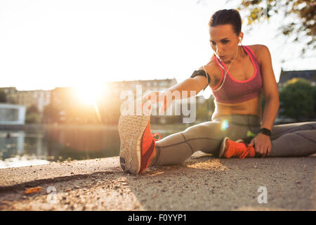 Fitness woman stretching before a run. Young female runner stretching her muscles before a training session. She is sitting on s