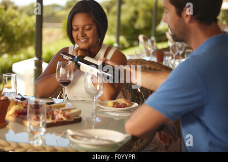 Man pouring a glass of red wine for his girlfriend at winery restaurant. Focus on woman sitting at table with her eyes closed. Stock Photo