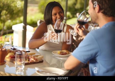 Young woman sitting at a table with her boyfriend drinking red wine. Happy young couple at wine bar restaurant. Stock Photo