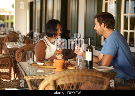 Male and female sitting at a restaurant holding glasses for wine and talking. Couple having a red wine at winery restaurant. Stock Photo
