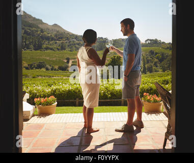 Young couple toasting wine while standing outdoors at winery restaurant patio. Man and woman on vacation celebrating with wine. Stock Photo