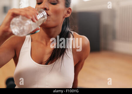 Close up shot of fitness woman drinking water in a break. Young female at gym taking a break after fitness training. Stock Photo