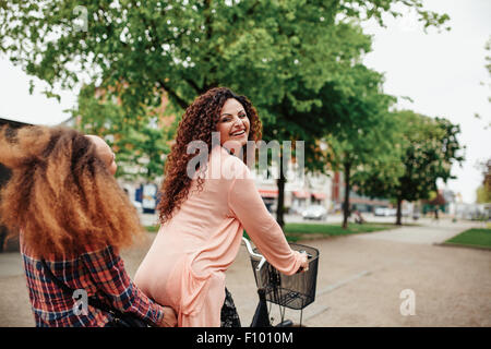 Portrait of beautiful young woman riding bicycle with her friend. Female friends having fun on cycle ride on city street.