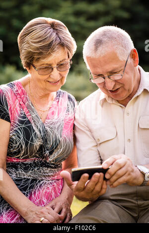Senior couple looking together on photos in smartphone - outdoor in nature Stock Photo